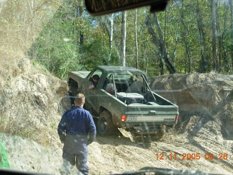 1987 Ford Bronco - A green off-road truck navigates a muddy trail, appearing stuck.