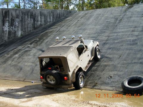 1987 Ford Bronco - A tan Jeep Wrangler ascends a steep concrete incline, its soft top partially open and spare tire visible on the rear.