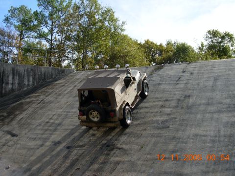 1987 Ford Bronco - Jeep Wrangler ascends a concrete slope, with trees and sky visible in the background.
