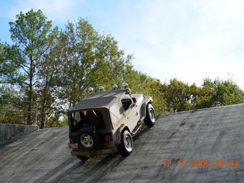 1987 Ford Bronco - A Jeep Wrangler ascends a concrete slope under a clear sky with trees in the background.