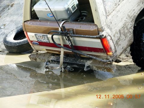 1987 Ford Bronco - This 1987 Ford Bronco is stuck in mud, showing its rear end with a spare tire and cooler in the cargo area.