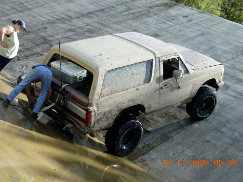 1987 Ford Bronco - This 1987 Ford Bronco is heavily covered in mud, with two people attending to the rear of the vehicle.