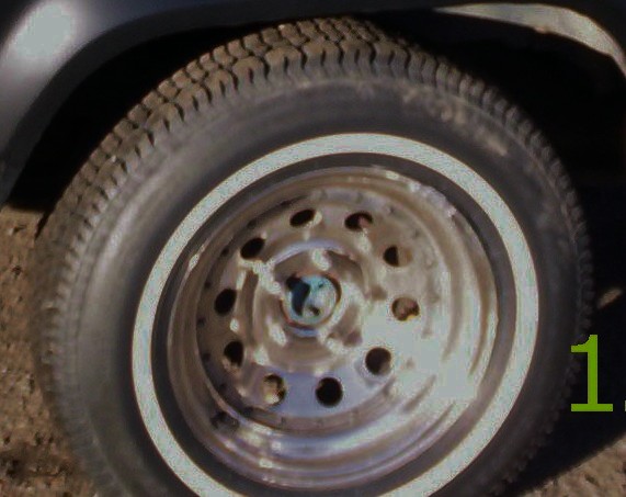 Close-up of a vehicle's wheel and tire, showing a silver rim with multiple holes and a white stripe on the tire