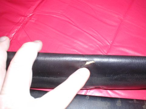 1979 Ford Bronco - Close-up of damaged black leather trim against a red background, with a finger indicating a tear.