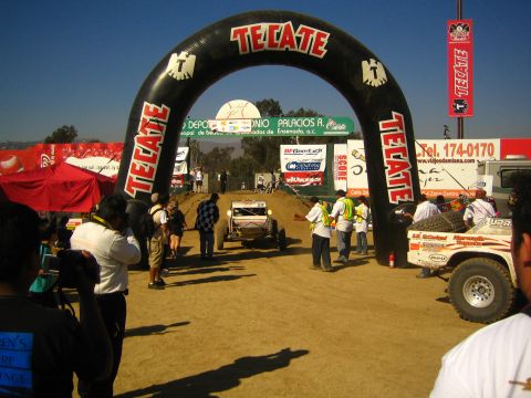 Race buggy heading toward an inflatable Tecate start arch on dirt