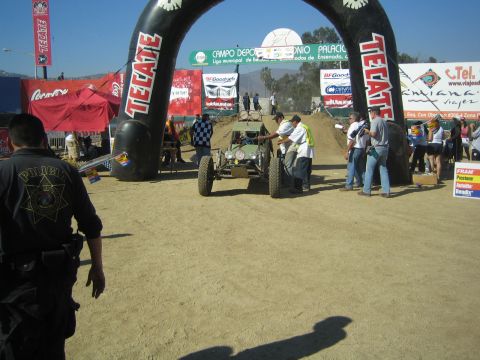 Green race buggy staged at an inflatable Tecate start arch with crew