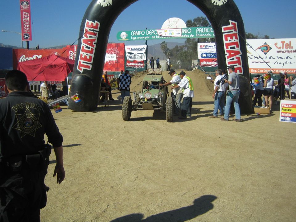 Green race buggy staged at an inflatable Tecate start arch with crew