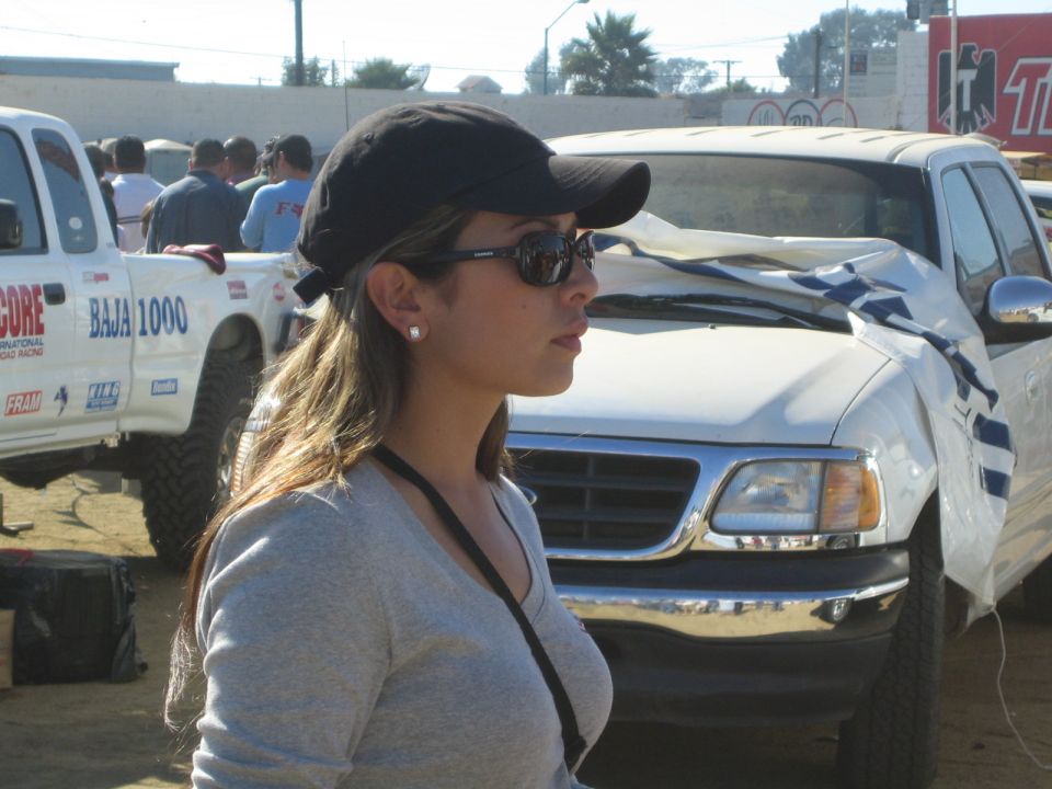 Young woman in cap and sunglasses beside a damaged white Baja 1000 truck