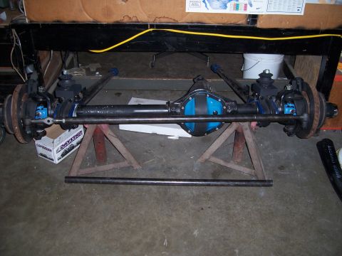 1983 Ford Bronco - A vehicle's front axle assembly, a blue differential cover, is supported by red jack stands in a garage.