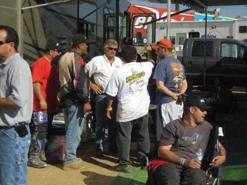 Group of men talking under a canopy beside an RV in a pit area