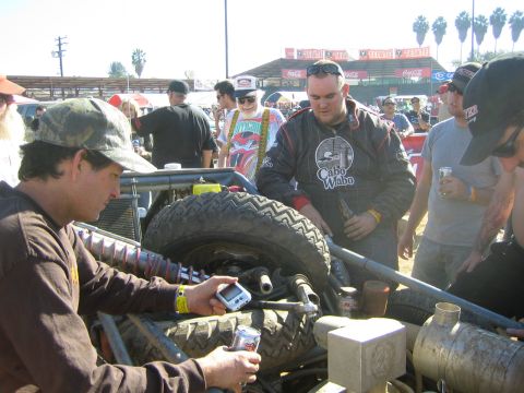 Men working on an off-road race vehicle's rear suspension in a sunny pit area
