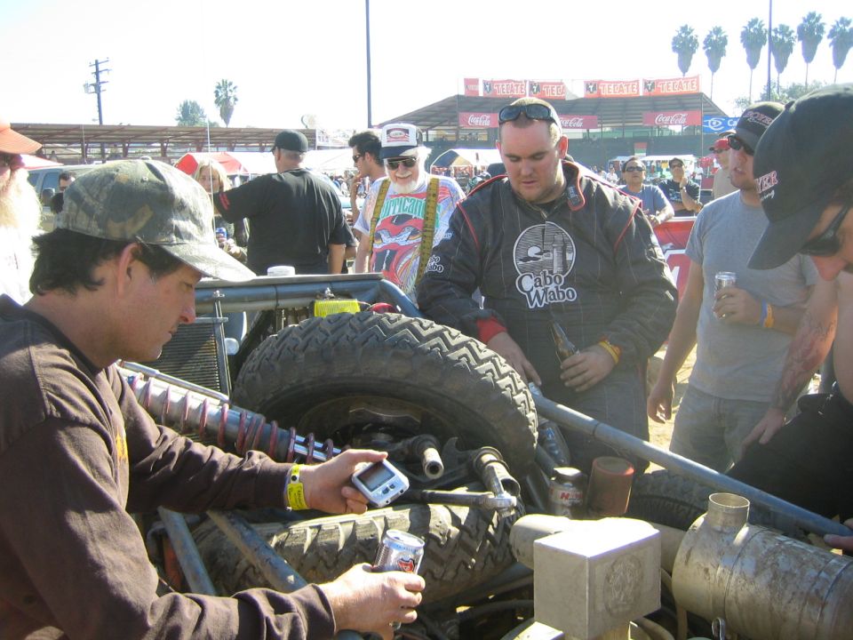 Men working on an off-road race vehicle's rear suspension in a sunny pit area