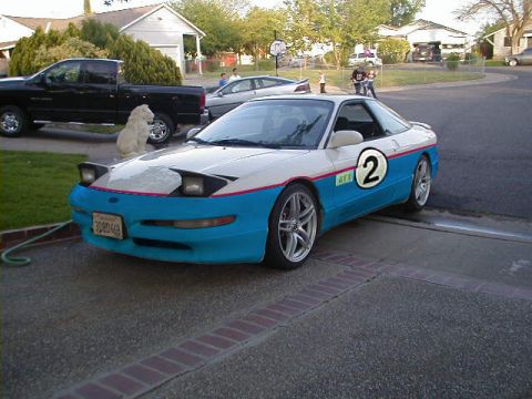 1997 Ford Probe - A two-tone Ford Probe with racing decals sits in a driveway next to a black pickup truck.
