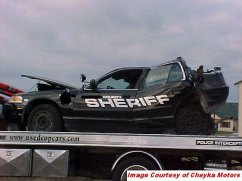 2000 Ford Crown Victoria - A heavily damaged sheriff's car is loaded onto a tow truck, showing extensive rear-end collision damage.