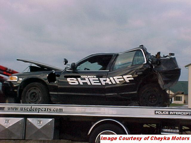 Damaged sheriff's car with 'COUNTY SHERIFF' text on the side, being towed