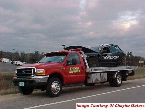 2000 Ford Crown Victoria - A red tow truck transports a damaged black police car with "SHERIFF" text on its door.