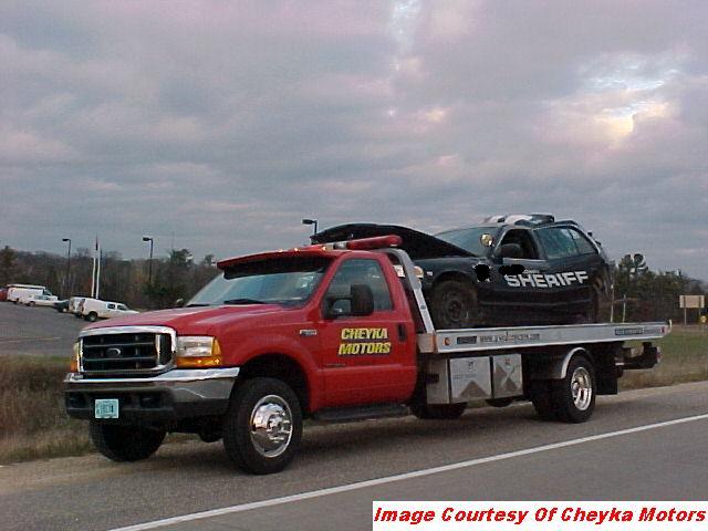 Black 2000 Ford Crown Victoria police car with "SHERIFF" on the side, loaded onto a red tow truck