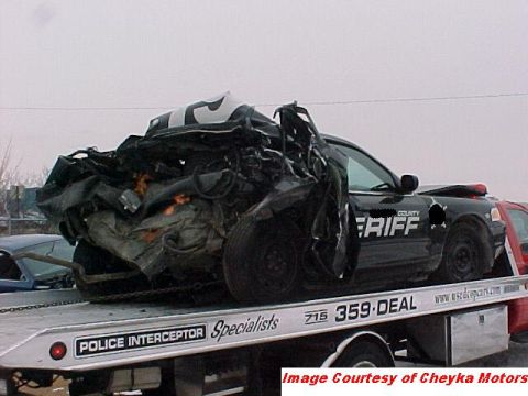 2000 Ford Crown Victoria - A severely damaged police car, identified as a 2000 Ford Crown Victoria, is loaded onto a tow truck.