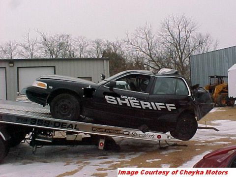 2000 Ford Crown Victoria - A damaged black 2000 Ford Crown Victoria, marked as County Sheriff, is loaded onto a tow truck.