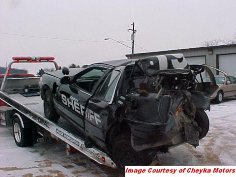 2000 Ford Crown Victoria - Severely damaged police car being towed, with another vehicle visible in the background.