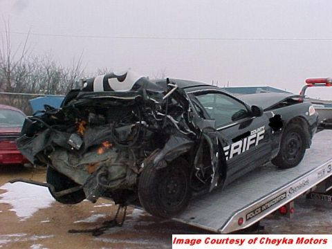 2000 Ford Crown Victoria - A severely damaged police car is being towed, its rear end completely crushed.