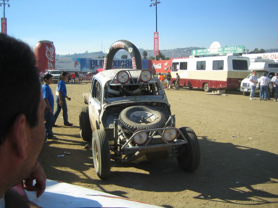 Stripped-body off-road race car with roof-mounted lights and front spare tire in a dirt lot