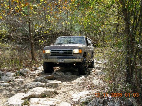 1987 Ford Bronco - 1987 Ford Bronco driving over rocks on a wooded trail.