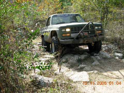 1987 Ford Bronco - This truck is navigating a rocky off-road trail surrounded by trees and foliage.
