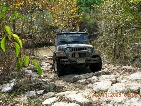 1987 Ford Bronco - A Jeep Wrangler navigates a challenging rocky path through an autumn forest.