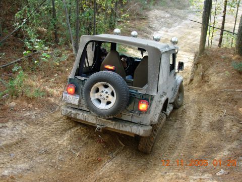 1987 Ford Bronco - A Jeep Wrangler TJ navigates a muddy, wooded trail. The vehicle is covered in dirt.