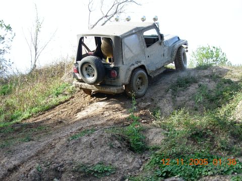 1987 Ford Bronco - A Jeep Wrangler navigates a muddy incline, kicking up dust.