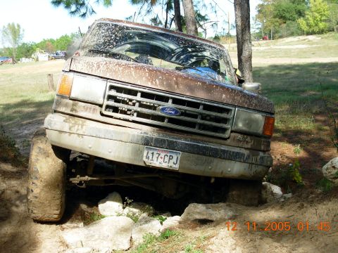 1987 Ford Bronco - A mud-covered 1987 Ford Bronco navigates a rocky off-road course.