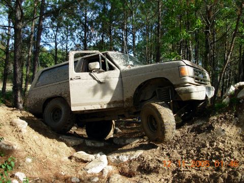 1987 Ford Bronco - This 1987 Ford Bronco is shown navigating a challenging off-road course covered in mud and rocks.