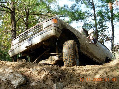 1987 Ford Bronco - A heavily mud-splattered Ford Bronco navigates a challenging off-road terrain.