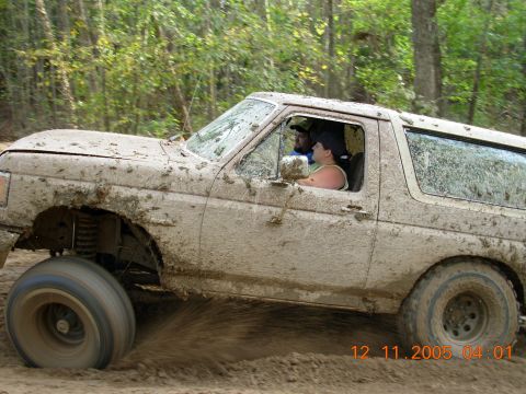 1987 Ford Bronco - A 1987 Ford Bronco navigates a muddy trail with two occupants inside.