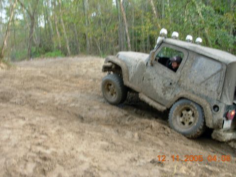 1987 Ford Bronco - A Jeep Wrangler navigates a muddy trail with trees in the background.