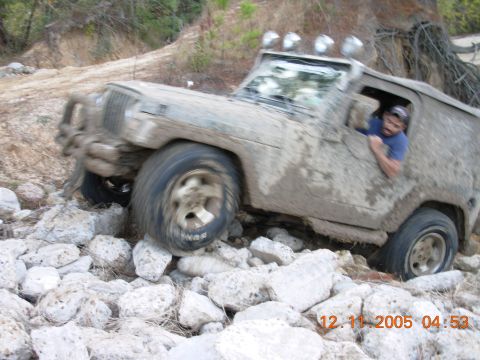 1987 Ford Bronco - A driver navigates a heavily muddied off-road vehicle over a challenging rocky path.