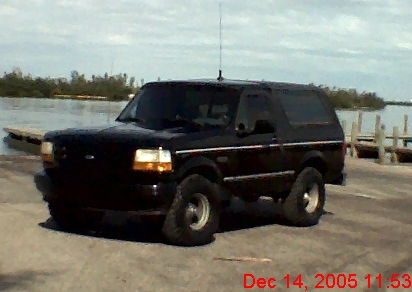 1993 Ford Bronco - A black Ford Bronco is parked on a paved surface near a body of water with a wooden dock.