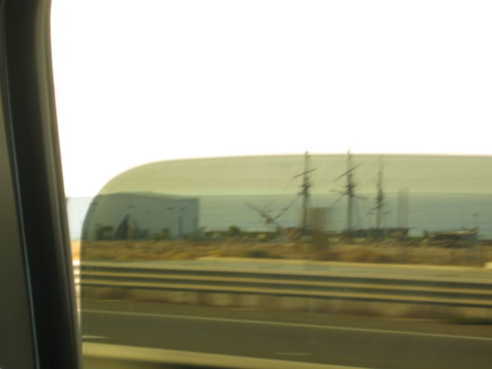 Blurry view of a tall ship's masts through a car window beside a highway