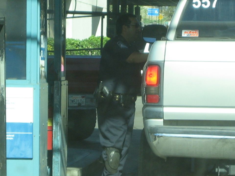 Uniformed officer standing beside a silver pickup at an inspection booth