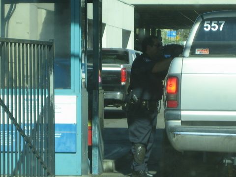 Officer leaning toward the window of a silver pickup at an inspection gate