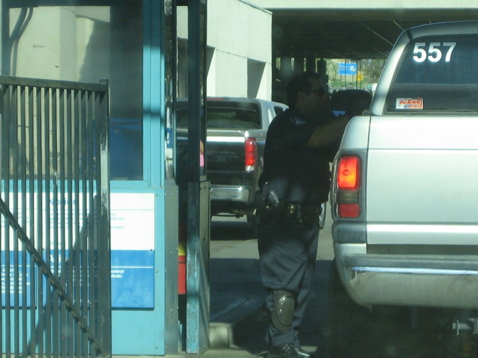 Officer leaning toward the window of a silver pickup at an inspection gate