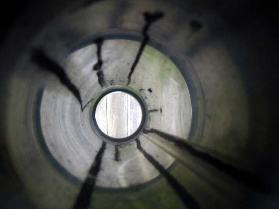 Exhaust pipe interior with carbon buildup and a view of wooden planks through the opening