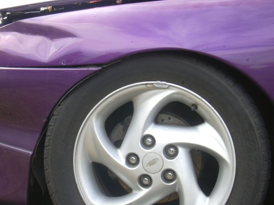 Purple 1997 Ford Probe fender with damage above the silver five-spoke wheel