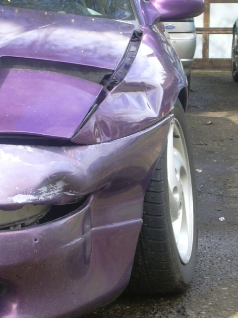 1997 Ford Probe - Front fender of a purple car shows significant damage, including dents and scraped paint, indicating a collision.