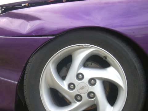 1997 Ford Probe - Close-up of a damaged purple 1997 Ford Probe fender and wheel.