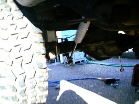 1987 Ford Bronco II - Underneath view of a vehicle's suspension components and tire, with tools nearby.