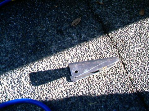 1987 Ford Bronco II - A metal bracket rests on a gravel surface, partially in shadow.