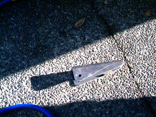Metal bracket with a hole, lying on a gravel surface with shadows
