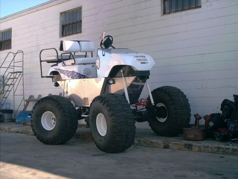 1991 Ford Bronco - A modified golf cart with massive tires sits in front of a white building.